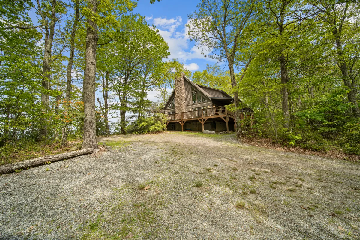An attractive A-frame cabin with a stone chimney sits amidst towering trees, illustrating the property’s harmonious integration with the natural environment. The peaceful exterior invites exploration and highlights the cabin’s secluded, storybook charm.