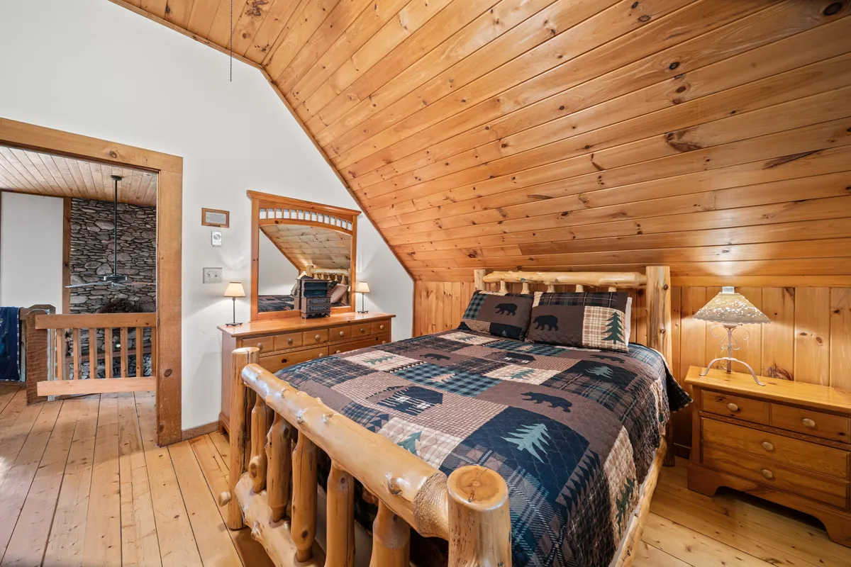A cozy bedroom featuring a log bed with a decorative quilt, wooden furnishings, and a wall-mounted mirror. Soft lighting and warm tones evoke a sense of comfort, ideal for unwinding after a day of activities.