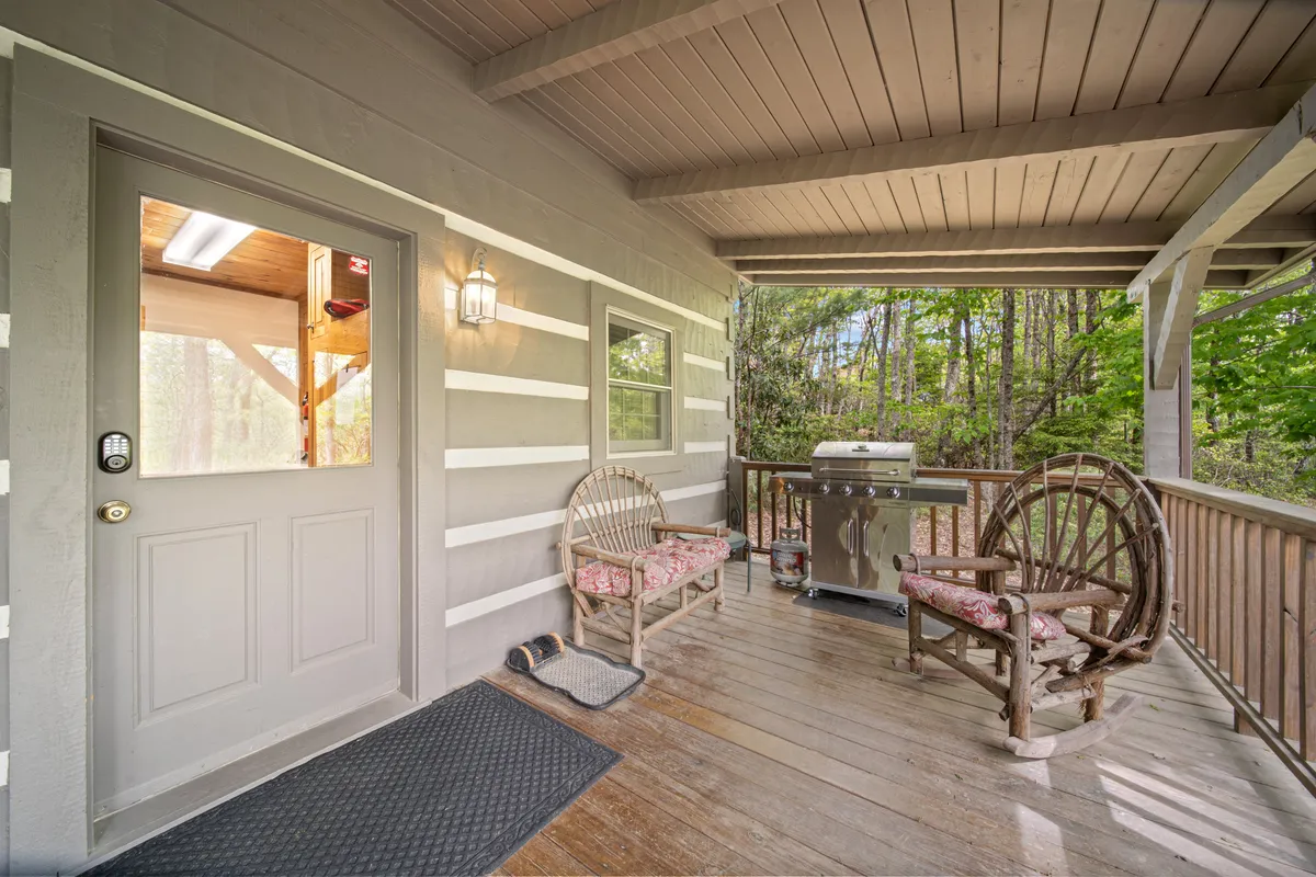 This exterior shot presents the front entrance area with wooden benches, a grill, and surrounding greenery. The scene suggests a welcoming, dog-friendly entry point and outdoor gathering space, ideal for socializing or enjoying a meal together after exploring the mountains.