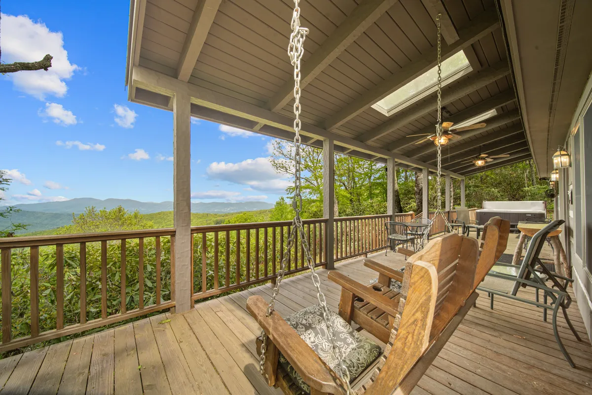 This exterior image showcases a spacious deck furnished with swinging chairs, ceiling fans, and an outdoor dining area, all overlooking a sweeping mountain view. The seating arrangement and openness invite guests to relax outdoors, enjoying the fresh mountain air and scenery.
