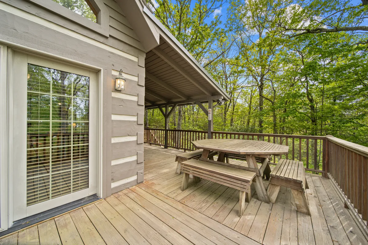An inviting wooden deck scene with a picnic-style dining table set near the railing, surrounded by forest and with views of the mountains in the background. The space is ready for al fresco meals and family gatherings, emphasizing outdoor living.