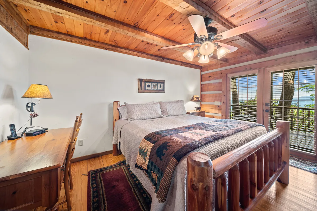 A king-sized bed with a patterned quilt is the centerpiece of a spacious room, complemented by a wooden desk and large windows that provide views of the outdoors. Warm lighting and inviting decor create an atmosphere of comfort and tranquility, ideal for relaxation.