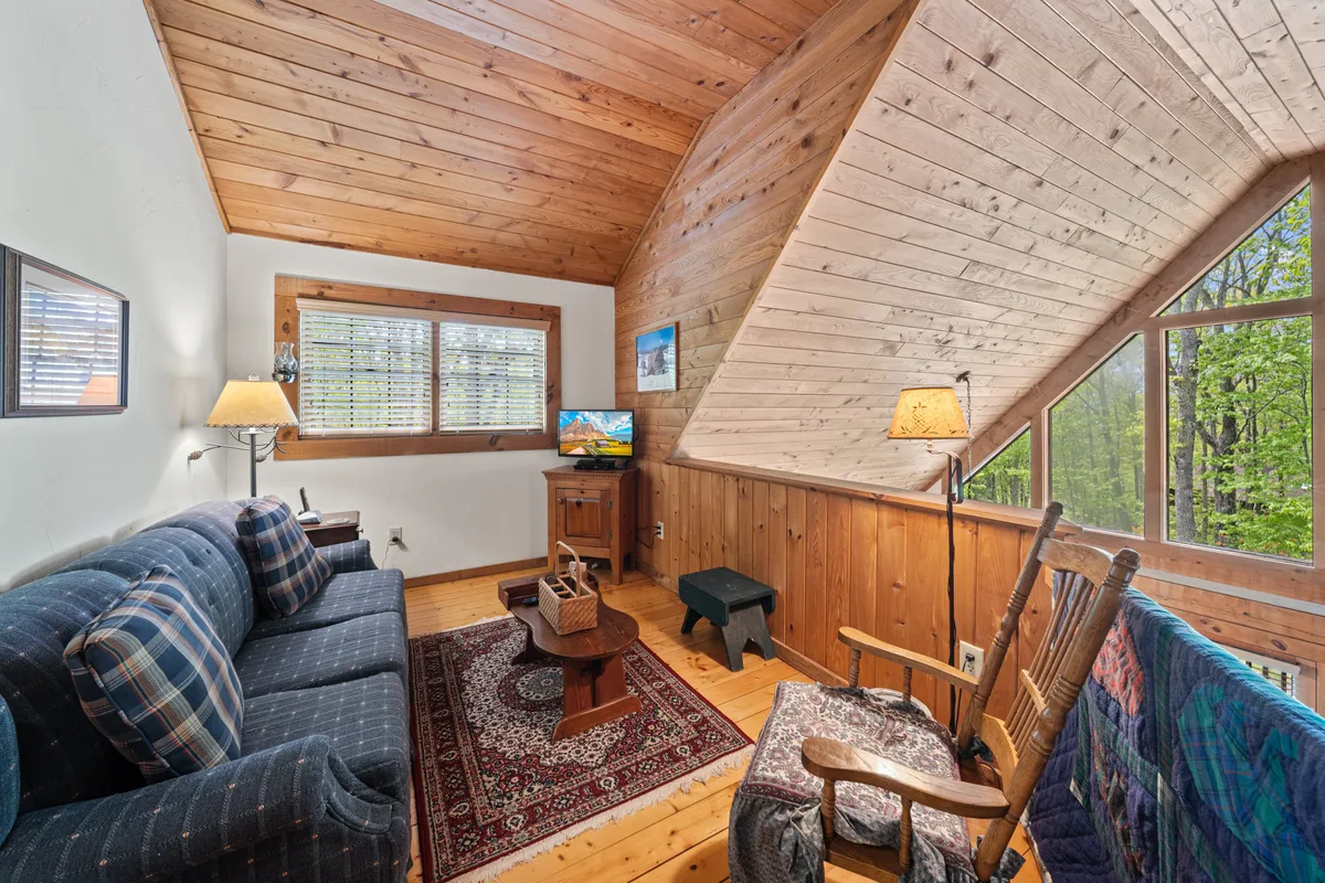 An inviting interior with a plush sofa, a rocking chair, a television, and a soft rug, all arranged in a warm, sunlit nook. The setup suggests a space ideal for curling up with a book, relaxing, or watching TV—perfect for guests seeking a cozy retreat.