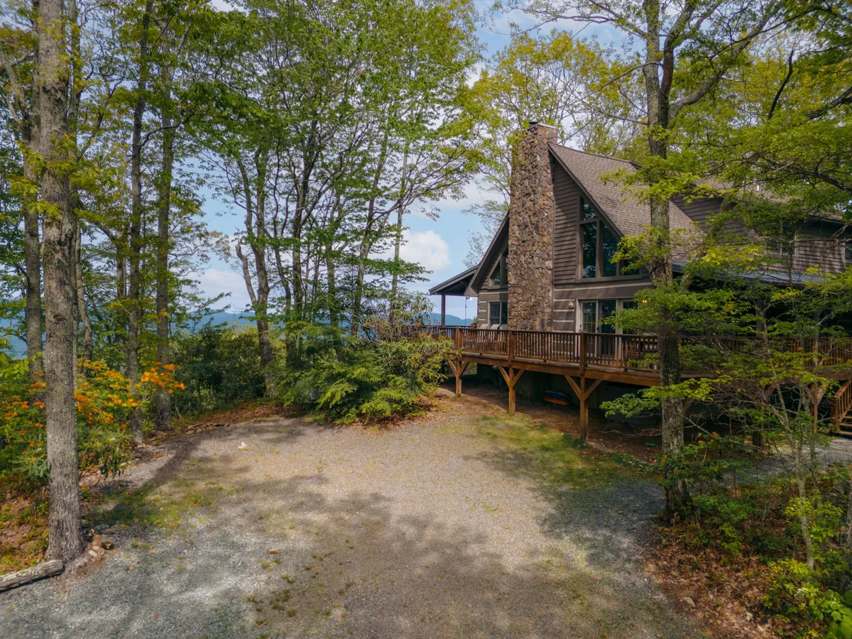 A tranquil exterior shot featuring a wooden deck, stone chimney, and an ample open area bordered by tall trees—ideal for children to play and families to gather. The image also hints at the serenity and adventure awaiting just beyond the property.