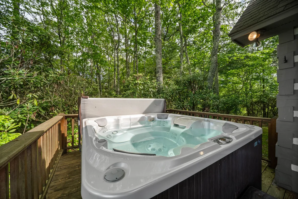 A different angle of the property’s exterior highlights the hot tub on a wooden deck framed by abundant greenery. The openness of the scene and the visible connection to the surrounding forest underline the immersive outdoor experience and the seamless integration of relaxation and exploration.
