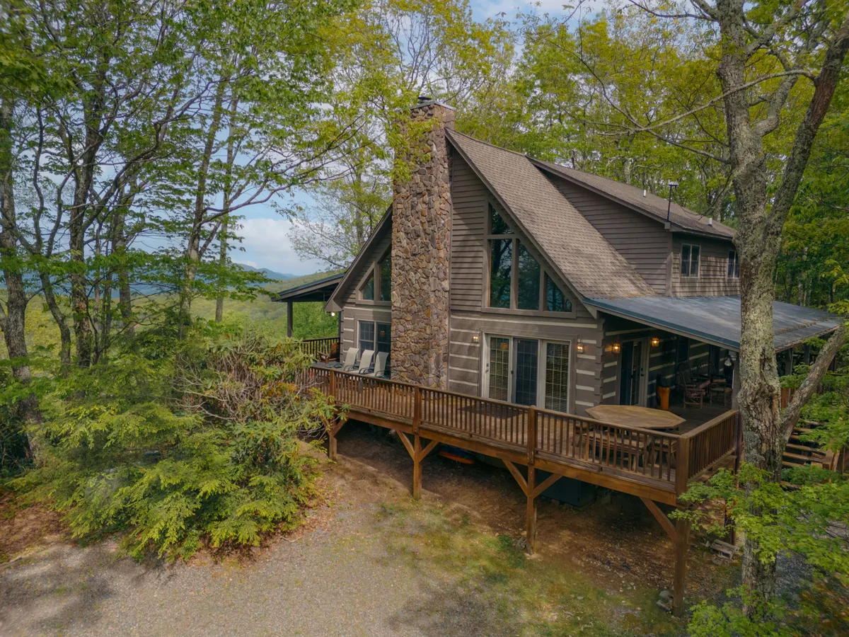 A wide view of a wooden deck attached to the home, featuring a stone chimney, large windows, and surrounded by lush trees. The deck is spacious and inviting, making it ideal for family outdoor activities and enjoying panoramic mountain views.